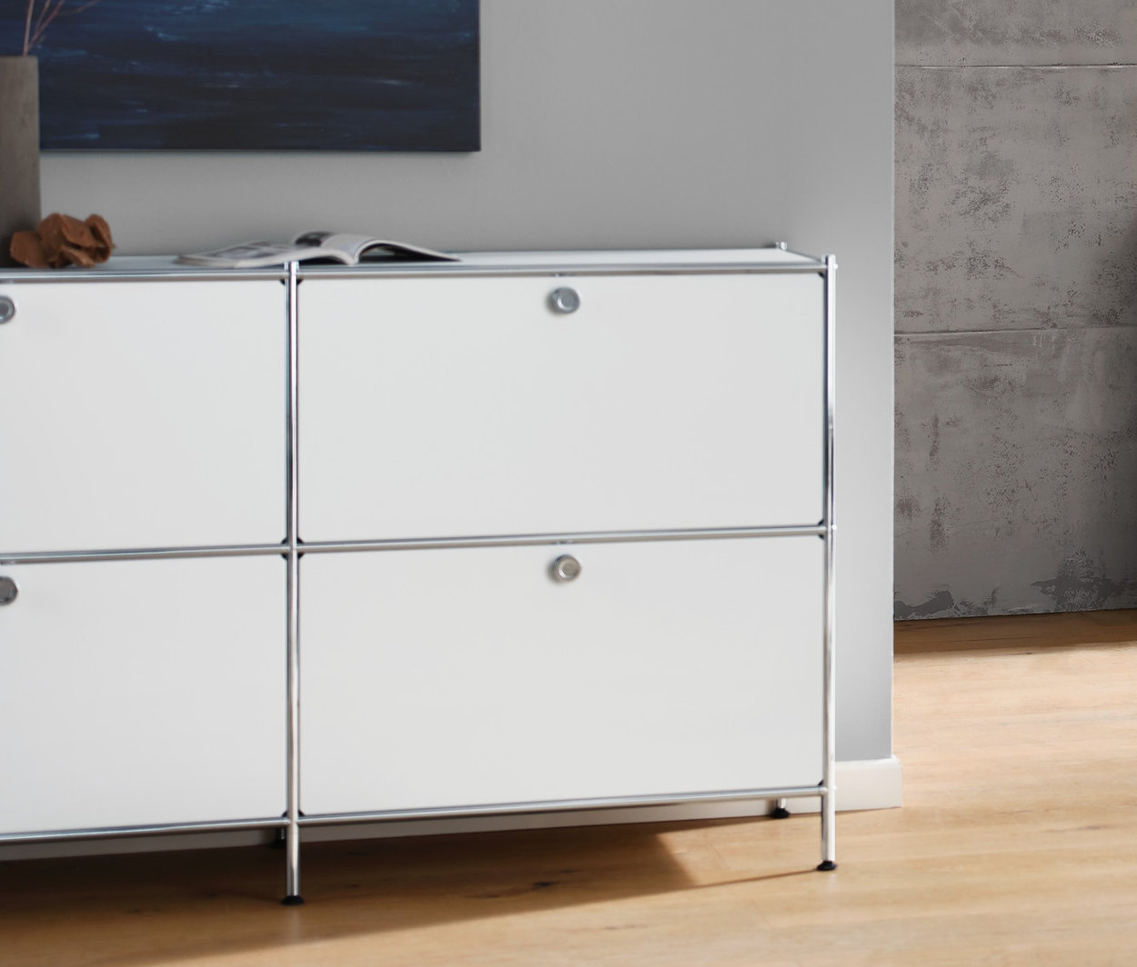 Obývací pokoj s bílou odkládací skříňkou CN3 se 6 výklopnými dvířky, antracitovou pohovkou pro 3 osoby, bílou stolní lampou s textilním stínidlem a bílým konferenčním stolkem CN3 s kolečky.