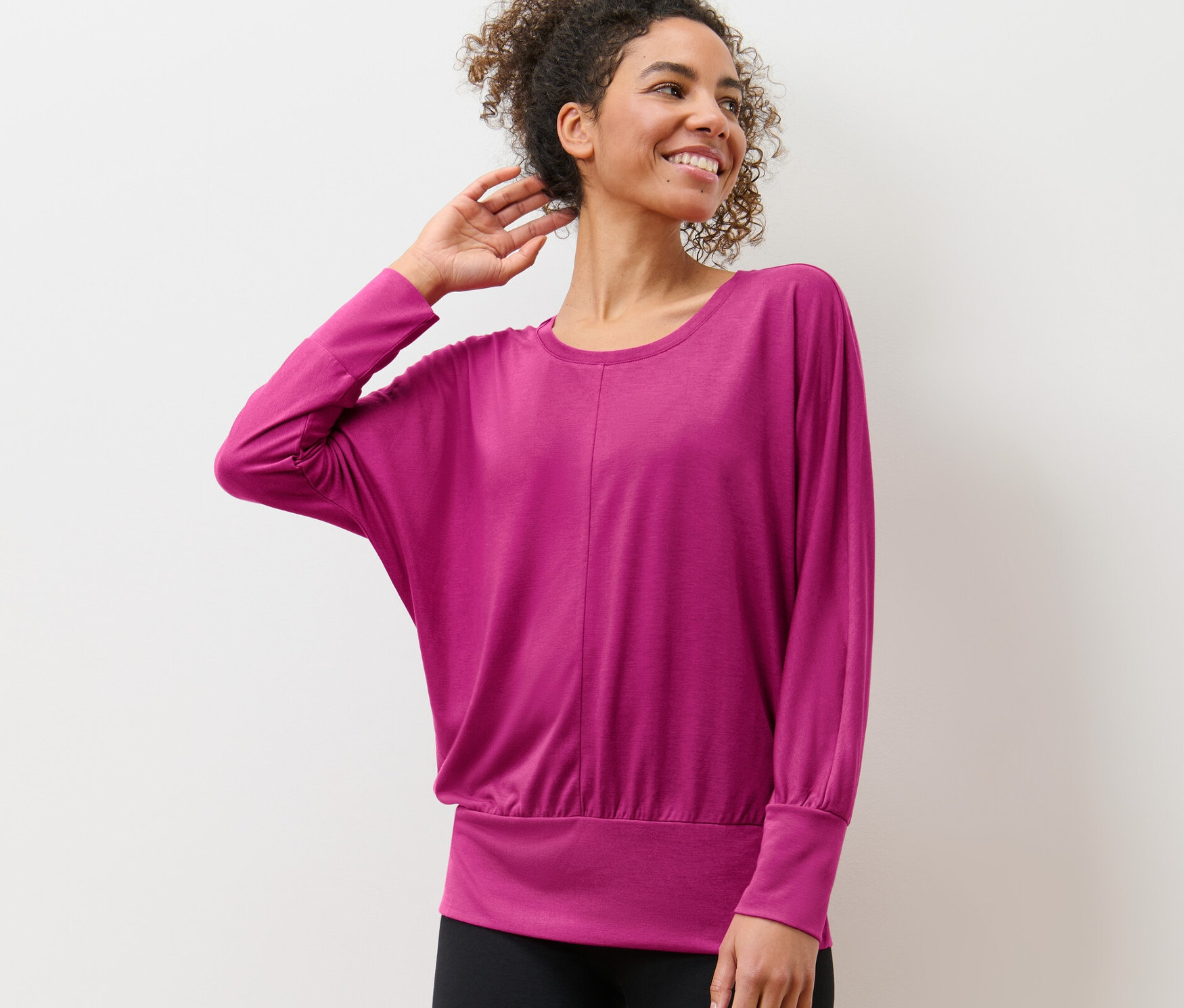 Žena v tričku na jógu pózuje před bílou zdí.