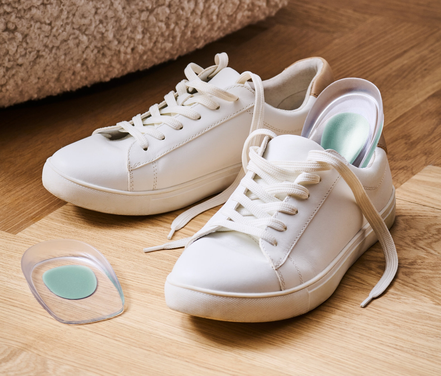 Dva bílé tenisky a jeden pár patních klínů na dřevěné podlaze.