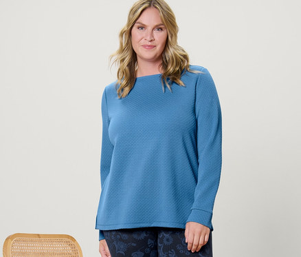 Žena pózuje vedle židle a má na sobě strukturovanou mikinu a legíny s potiskem.