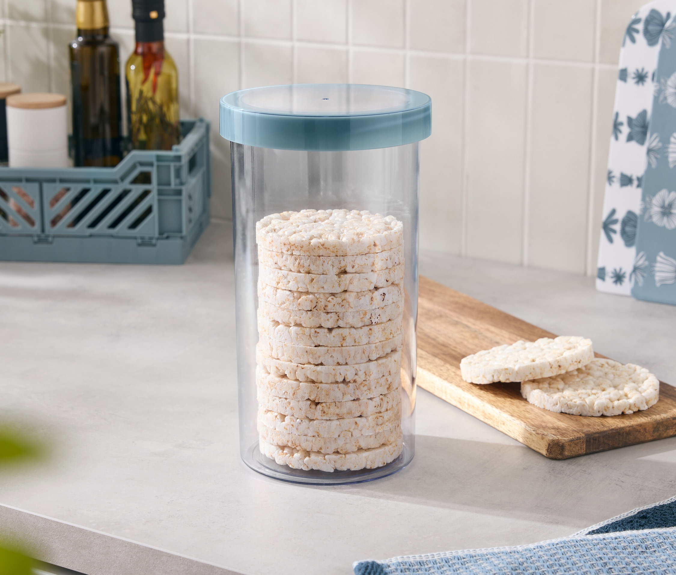 V dóze s modrým víkem je naskládáno několik rýžových koláčků, dva další leží na dřevěném prkénku.