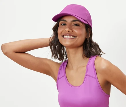 Žena pózuje ve sportovní podprsence a sportovní kšiltovce.