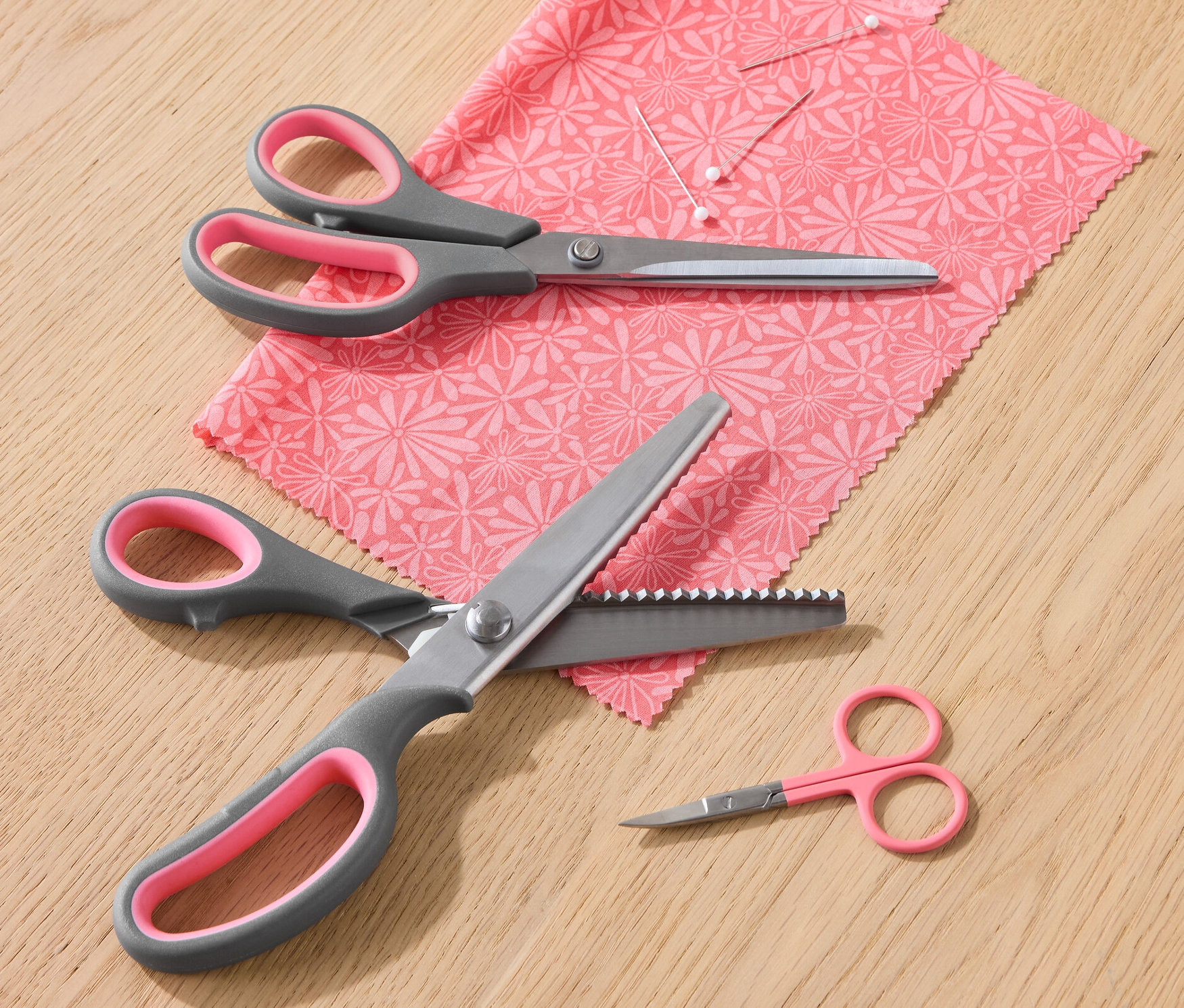 Sada nůžek na textil leží na kousku látky s květinovým vzorem.