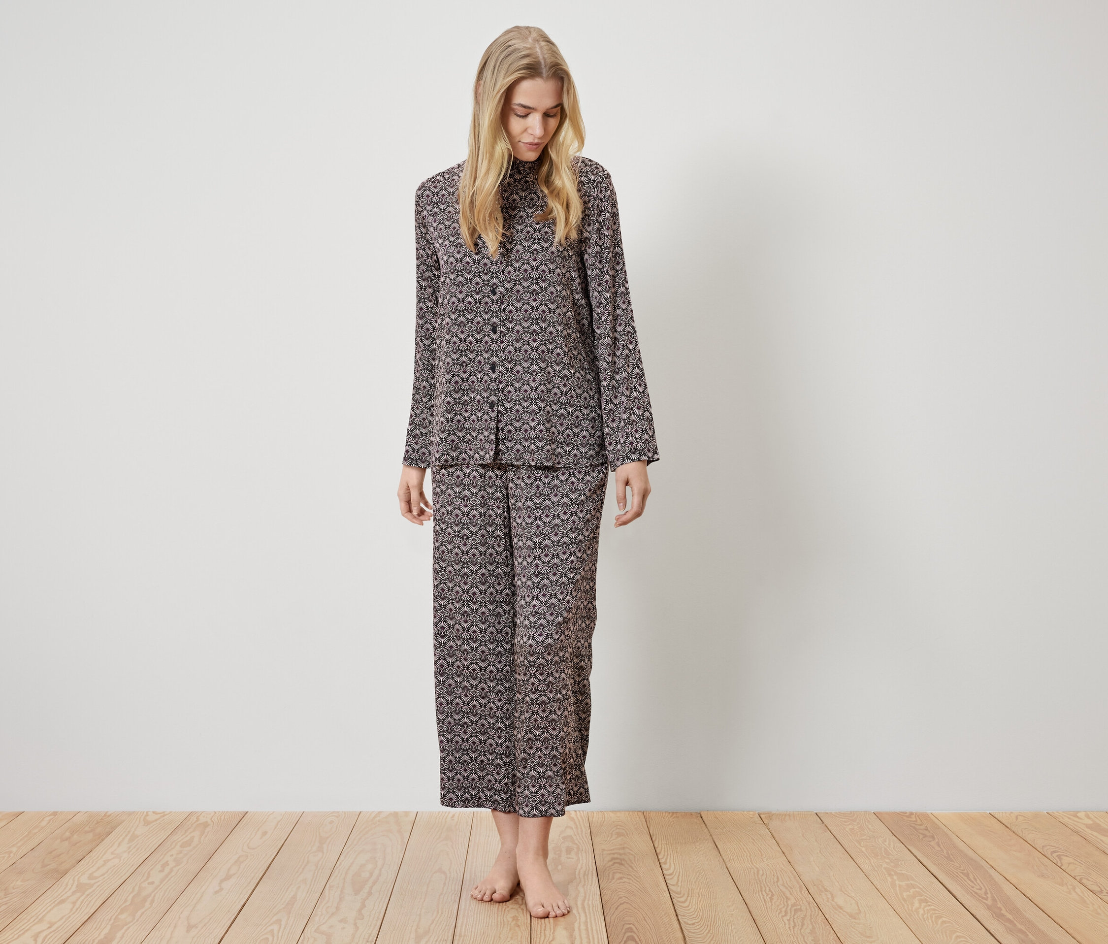 Žena stojí a má na sobě hnědé pyžamo se vzorem.