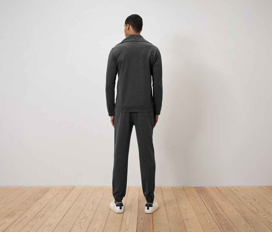 Muž zády k fotoaparátu má na sobě tmavě šedý teplákový oblek a bílé tenisky.