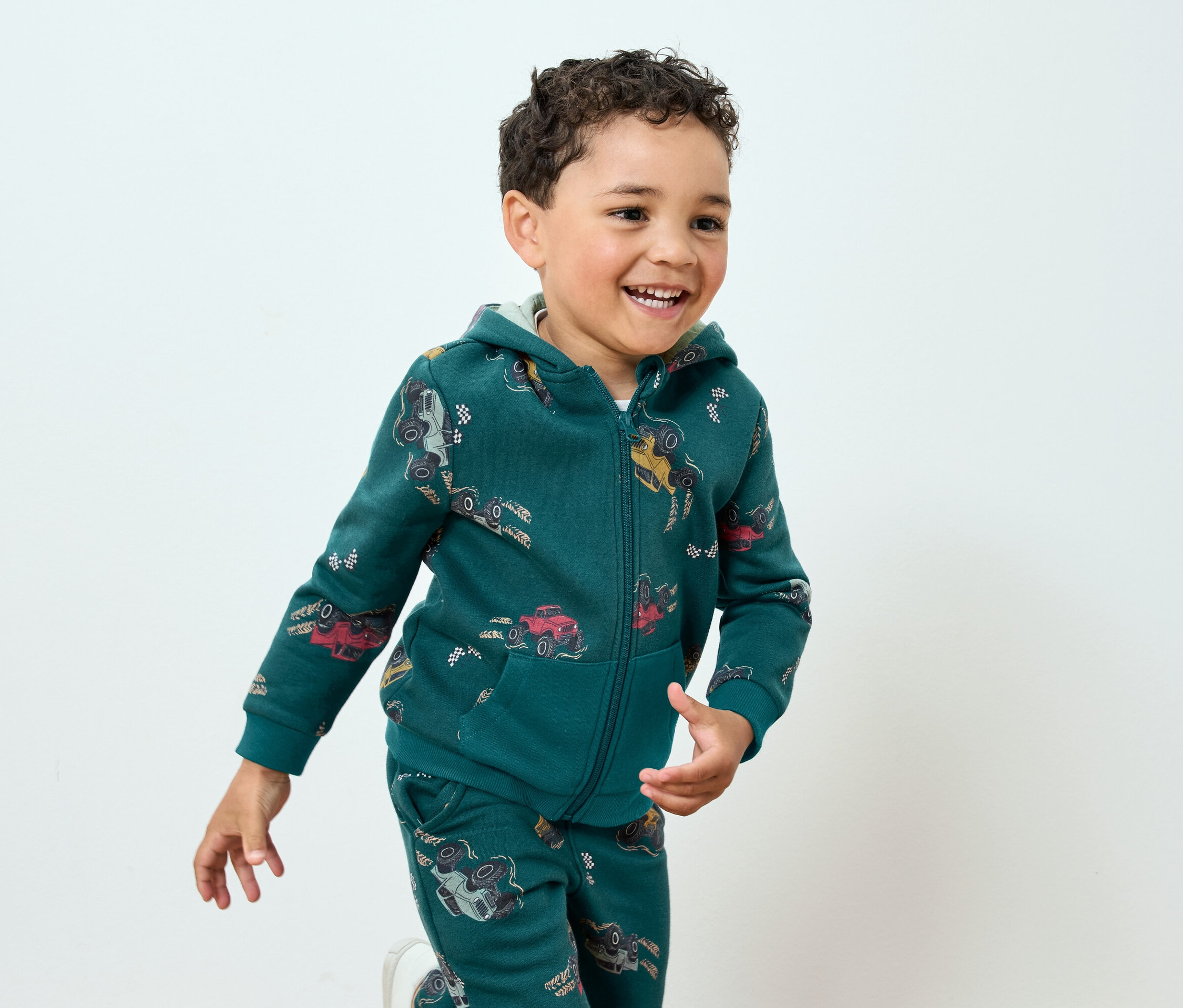 Usmívající se chlapec v zelené soupravě s potiskem aut