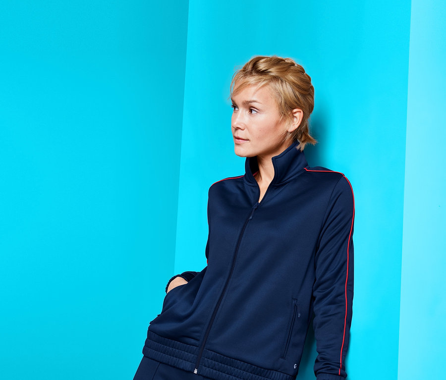 Žena pózuje v tmavě modré sportovní bundě.