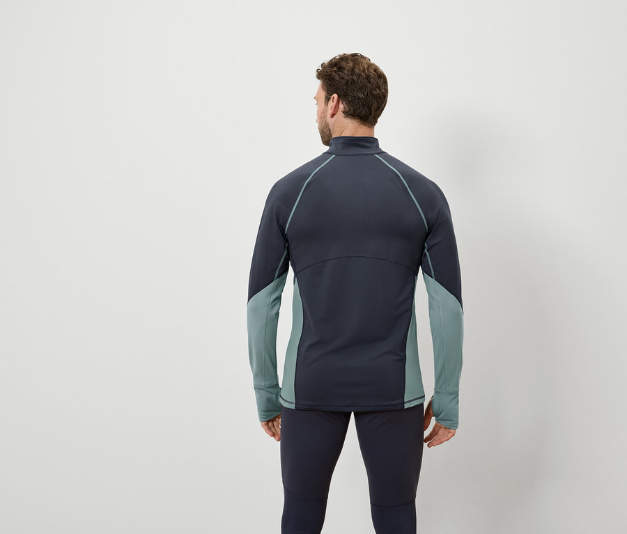 Muž zády k fotoaparátu má na sobě tmavě modrý top s dlouhým rukávem a šedozelenými panely a tmavě modré legíny.