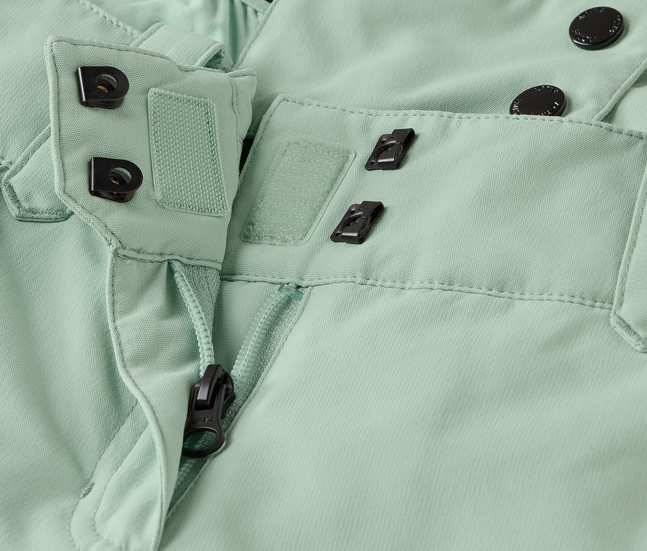 Detail světle zelených kalhot se zipem a zapínáním na knoflíky.