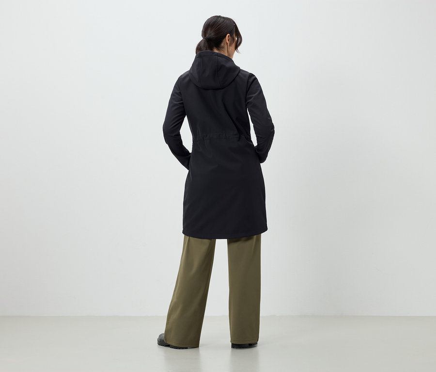 Žena zády k fotoaparátu má na sobě černý kabát a zelené kalhoty.