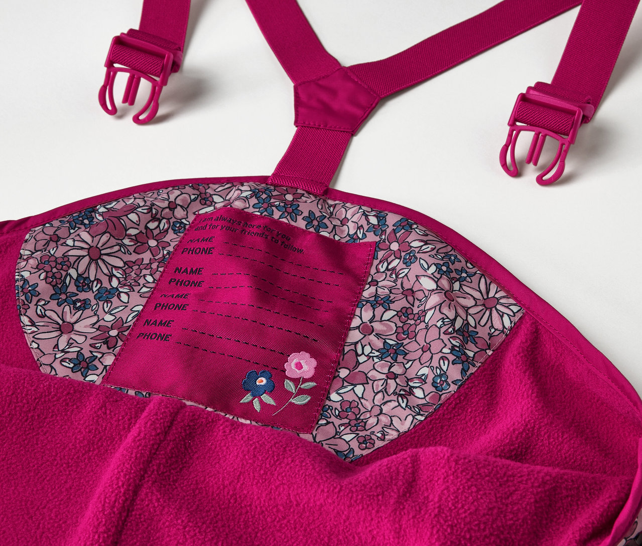 Detail dětských termo kalhot do deště s květinovým vzorem, včetně detailů jako jsou ramenní popruhy a štítek na jméno.