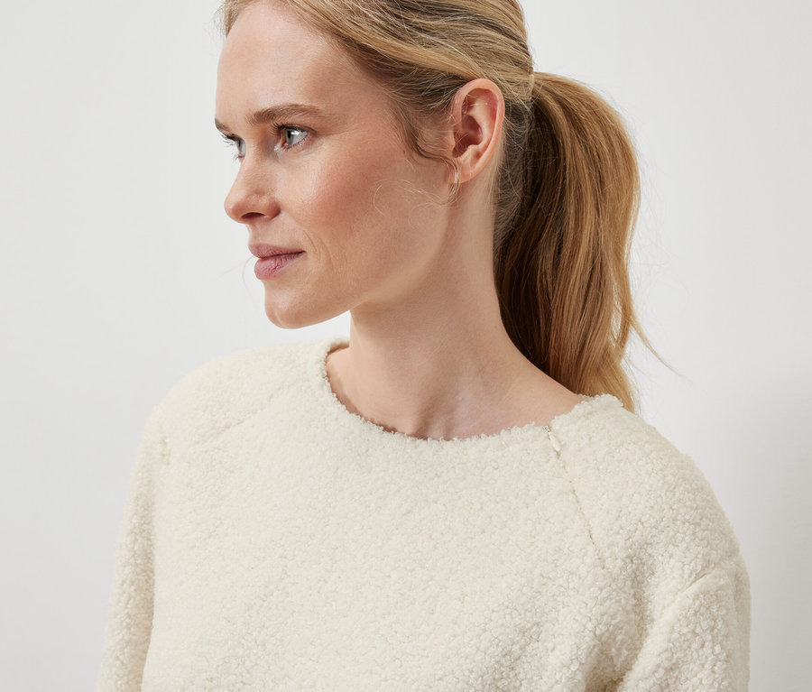 Detail profilu blondýny s vlasy staženými do culíku, která má na sobě krémový svetr.