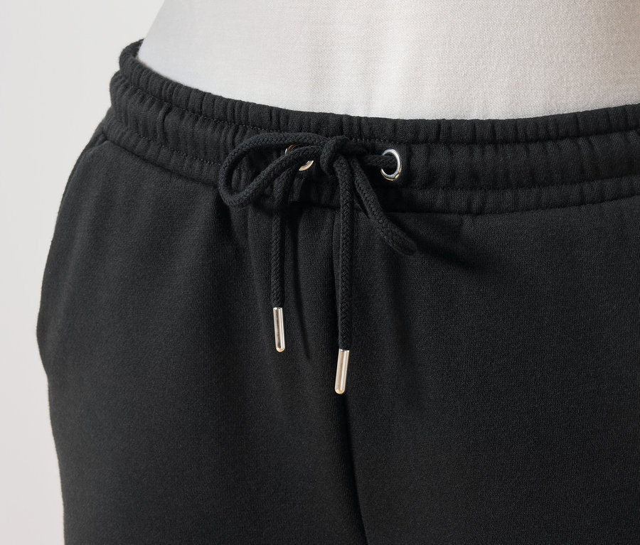 Detail černých tepláků se stahovací šňůrkou v pase.