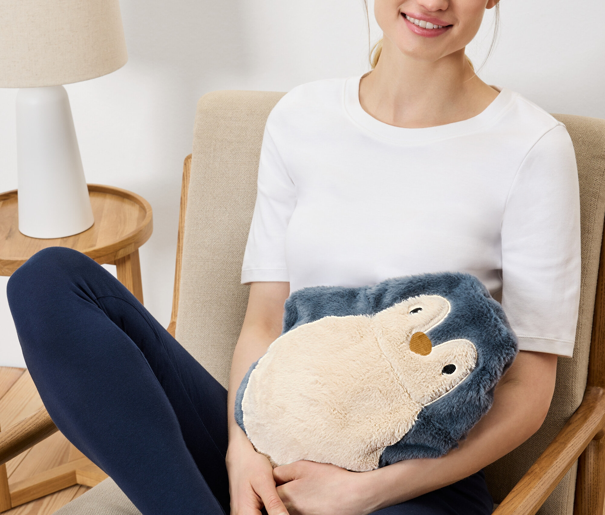 Žena sedí v křesle a drží plyšového hřejivého tučňáka.