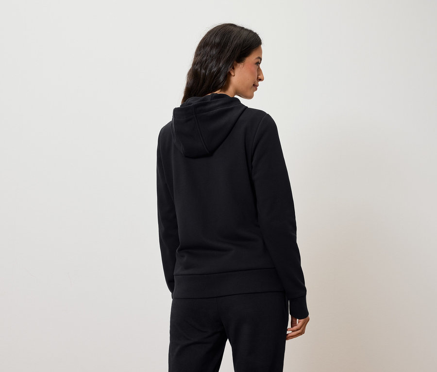 Žena z pohledu zezadu má na sobě černou mikinu s kapucí a černé kalhoty.