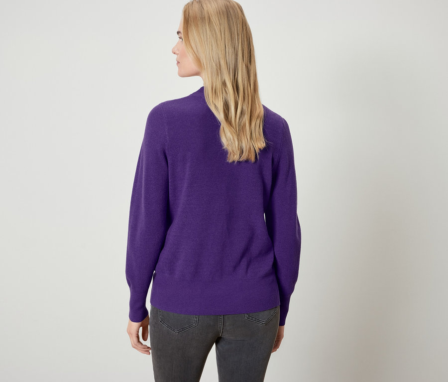 Zezadu je vidět žena s blond vlasy v purpurovém svetru a šedých džínách.