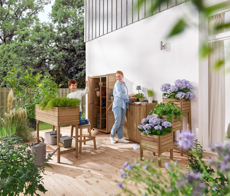 Chlapec a žena manipulují se zahradním nábytkem a rostlinami na dřevěné terase.