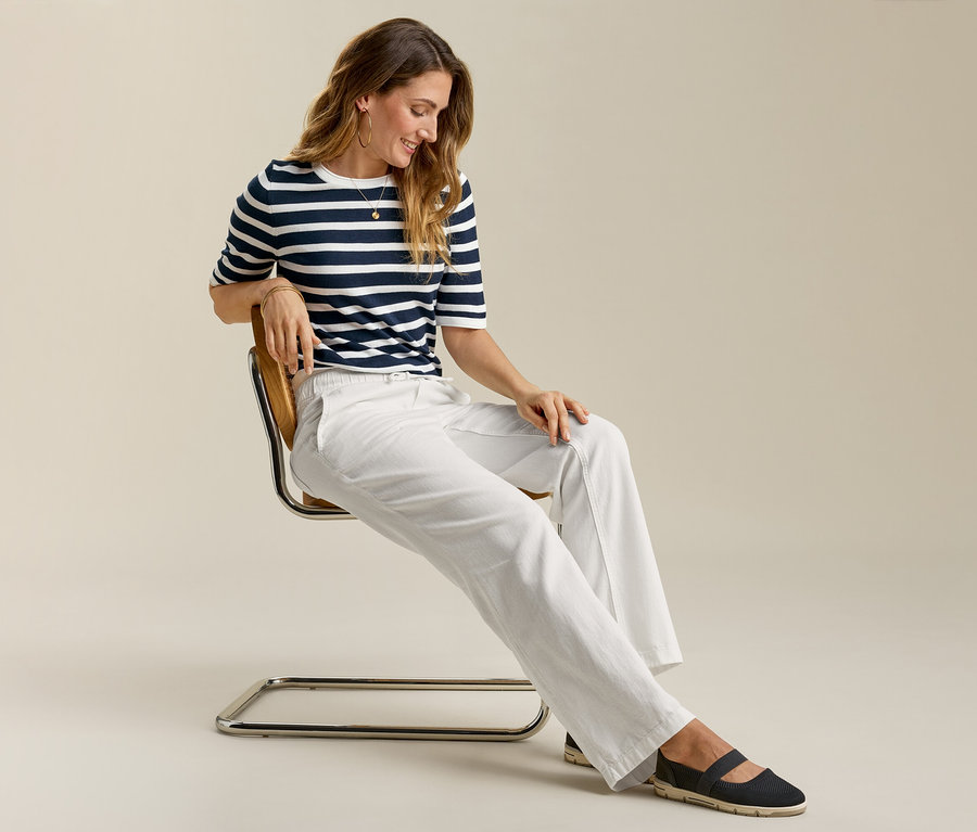Žena sedí na židli a má na sobě Pohodlné široké džíny, pruhované tričko a baleríny.