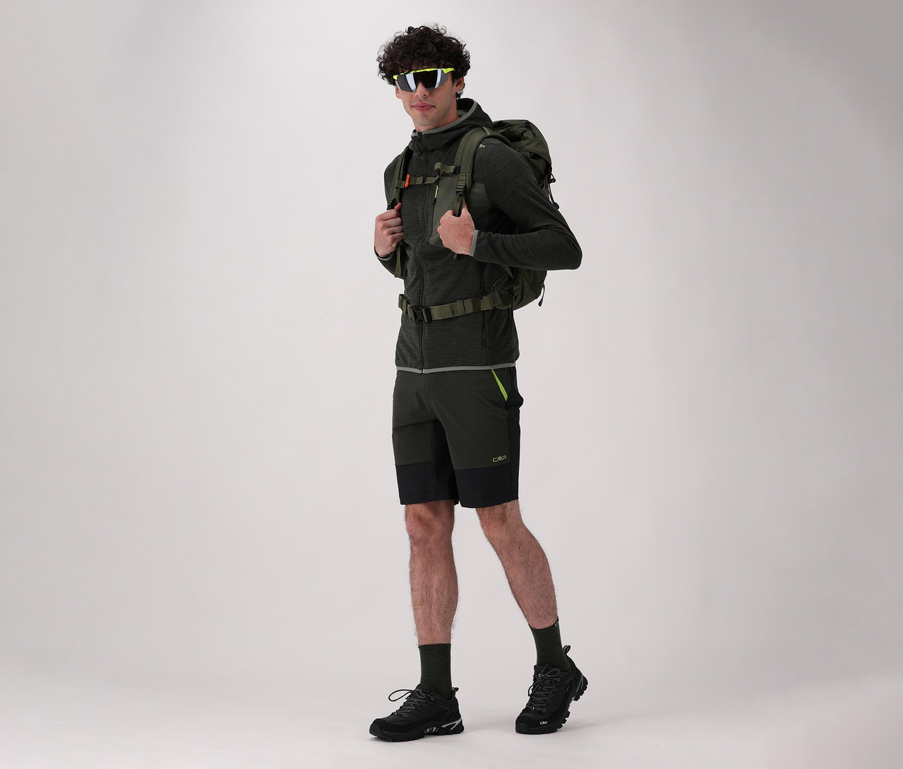 Muž s batohem a v černých trekových botách CMP RIGEL LOW 2.0 WP pózuje na světlém pozadí.