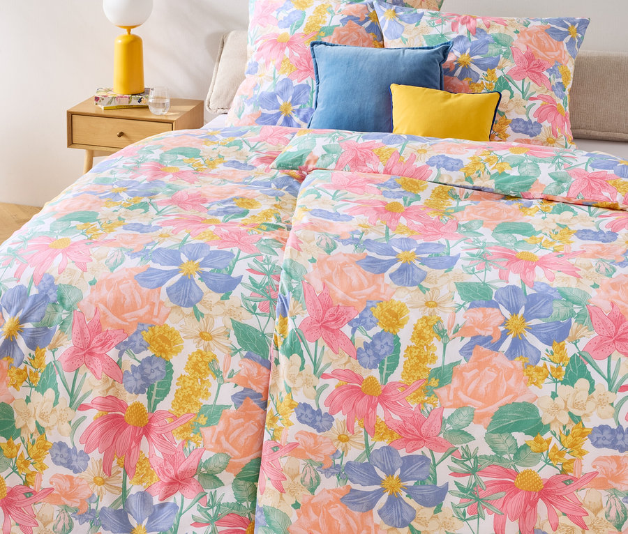 Květinové ložní prádlo Renforcé, dvojitá, standardní a nadměrná velikost na posteli s modrými a žlutými polštáři.