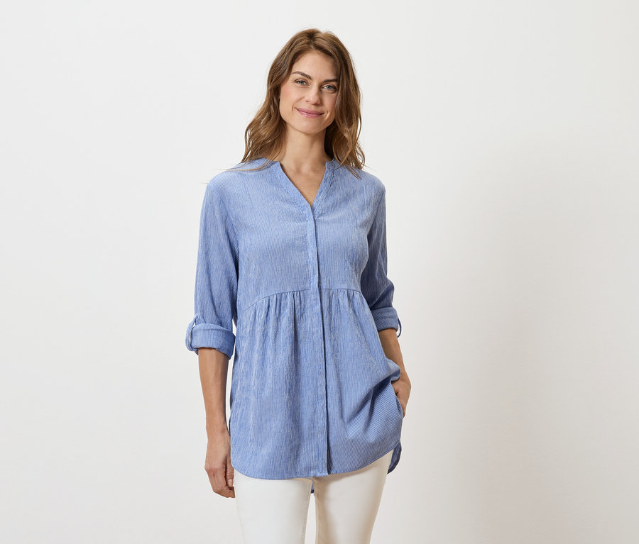 Žena má na sobě světle modrou halenku s dlouhým rukávem a bílé kalhoty.