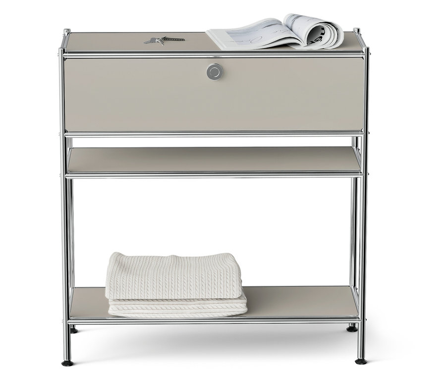 Na třípatrové polici s chromovaným rámem leží nahoře klíč a časopis a dole leží složené dvě bílé deky.