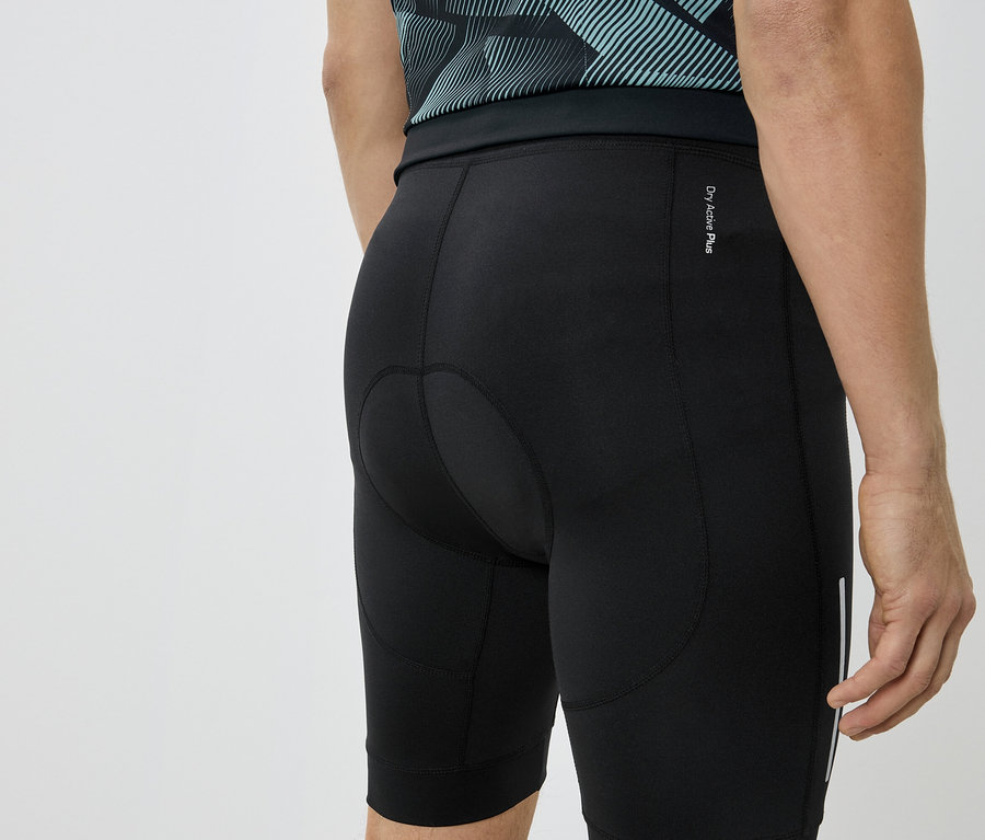 Detailní záběr na zadní část osoby v černých cyklistických šortkách a modrozeleném tričku.