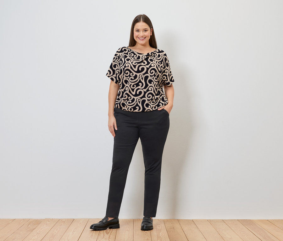 Žena ve vzorované halence a kalhotách joggpant s rukou v kapse.