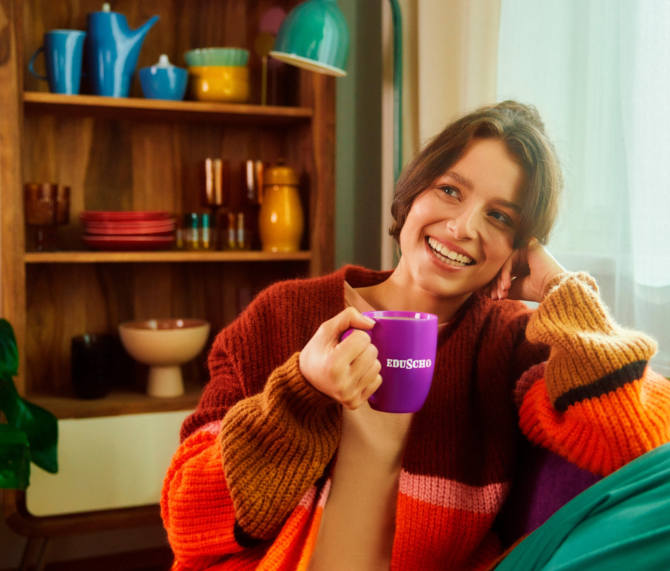 Usmívající se brunetka drží fialový hrnek s nápisem EDUSCHO. V pozadí je police s nádobím.
