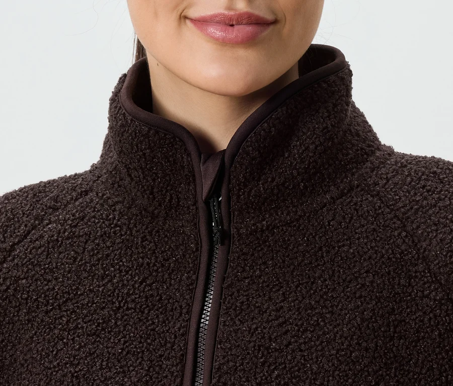 Detailní záběr na ženu v hnědé fleecové bundě na zip s vysokým límcem.