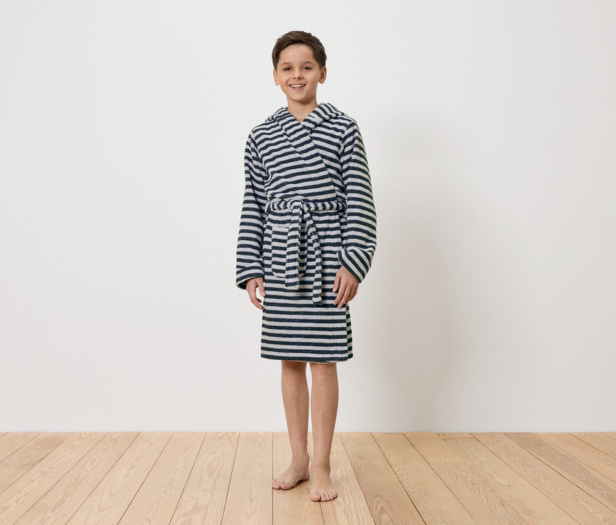 Chlapec stojí bosý před bílou stěnou a má na sobě pruhovaný župan s kapucí.