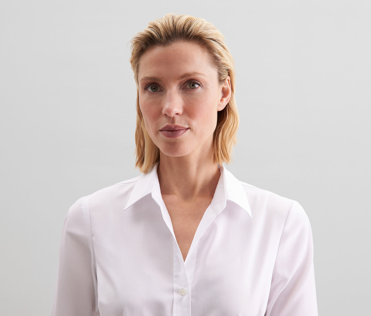 Žena s blond vlasy má na sobě bílou halenku slim fit non iron Seidensticker.