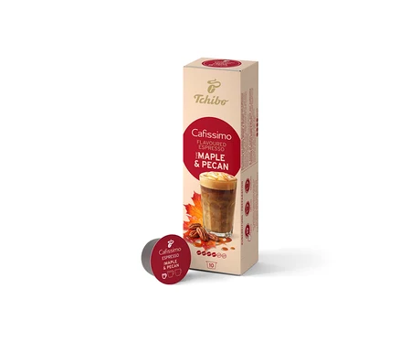 Béžová krabička Cafissimo Flavoured Espresso Maple & Pecan (10 kapslí) stojí vzpřímeně, před ní leží jedna tmavě červená kapsle. Krabička zobrazuje kávový nápoj, javorové listy a pekanové ořechy.