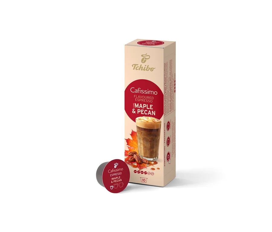 Béžová krabička Cafissimo Flavoured Espresso Maple & Pecan (10 kapslí) stojí vzpřímeně, před ní leží jedna tmavě červená kapsle. Krabička zobrazuje kávový nápoj, javorové listy a pekanové ořechy.