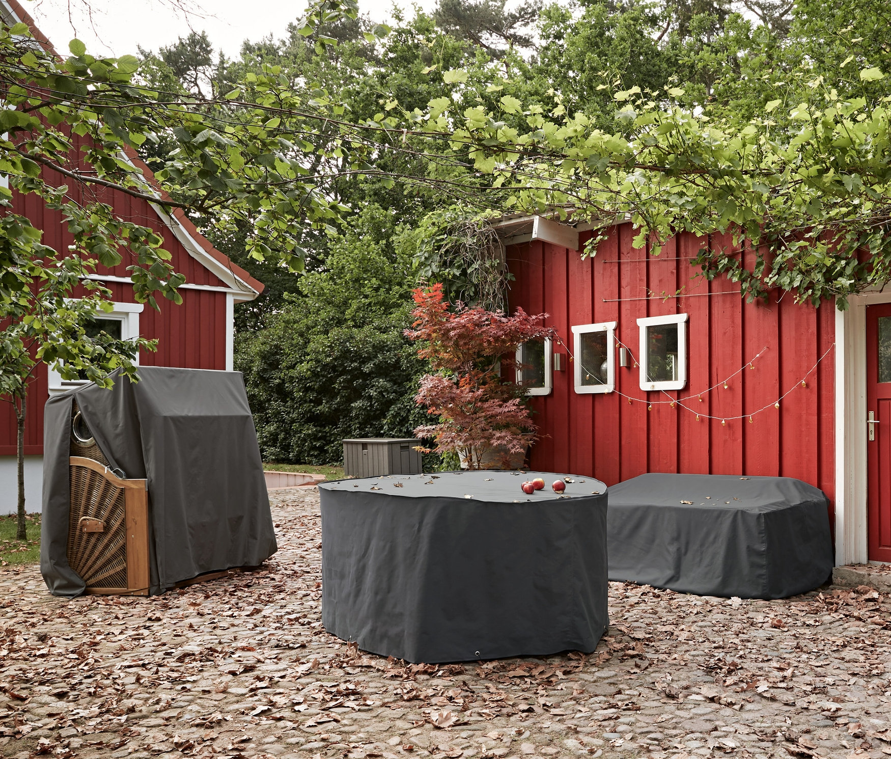 Na dlážděné terase jsou umístěny prémiové ochranné kryty na jídelní soupravu, lounge nábytek "Zahradní pohovka" a plážový koš.