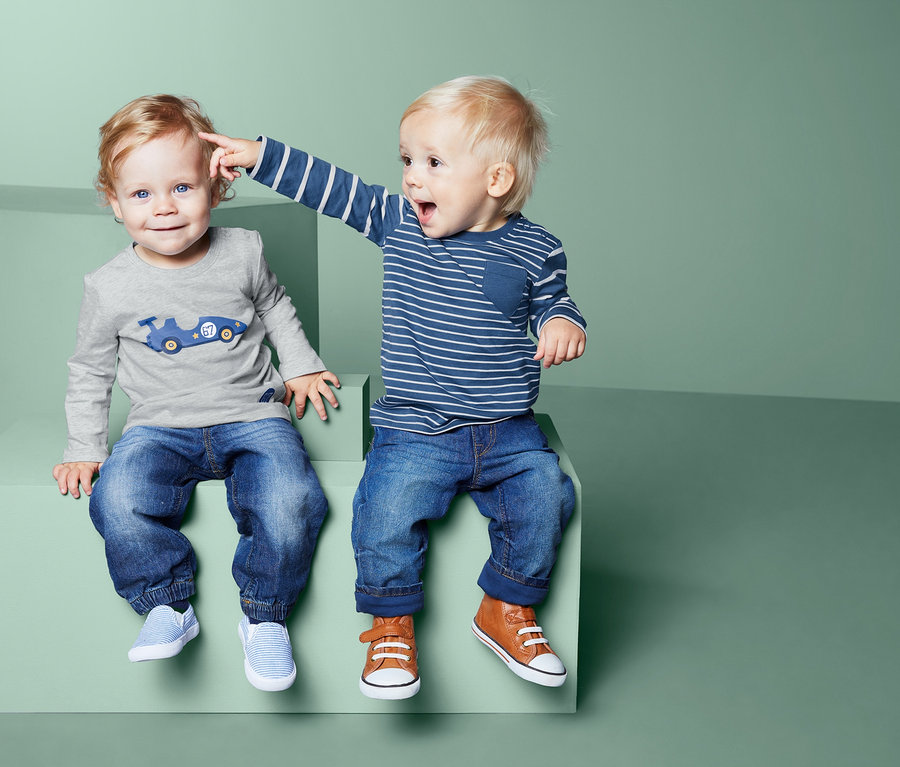 Dva chlapci sedí na zelených kostkách. Jeden ukazuje prstem na hlavu druhého. Oba mají na sobě džíny a trička s dlouhým rukávem, 2 ks.