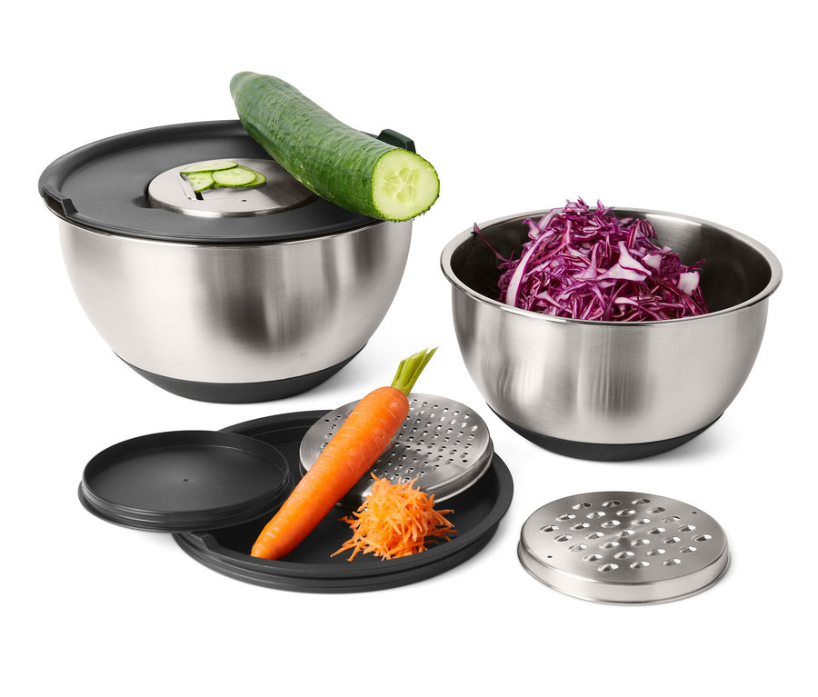 Nerezové mísy na pozadí s okurkou, červeným zelím a mrkví na struhadle.