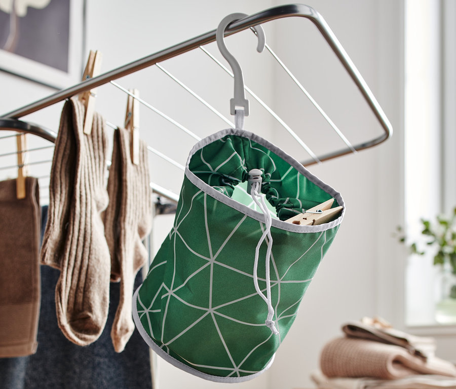 Zelený sáček na kolíčky visí na sušáku prádla, který je plný prádla.
