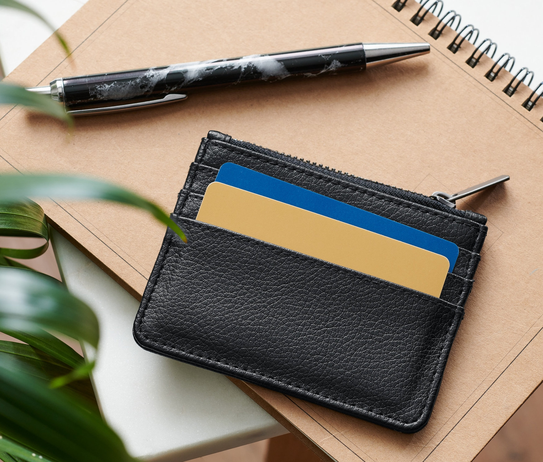 Černé pouzdro na karty leží na poznámkovém bloku vedle pera.
