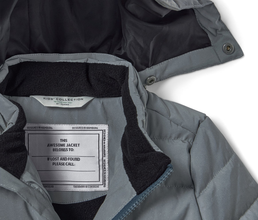 Detail šedé dětské prošívané bundy s kapucí a reflexními prvky.