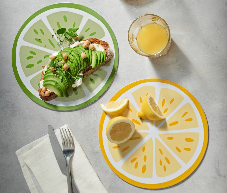 Toast s avokádem na zeleném prkénku na snídani, vedle džbán a sklenice džusu.