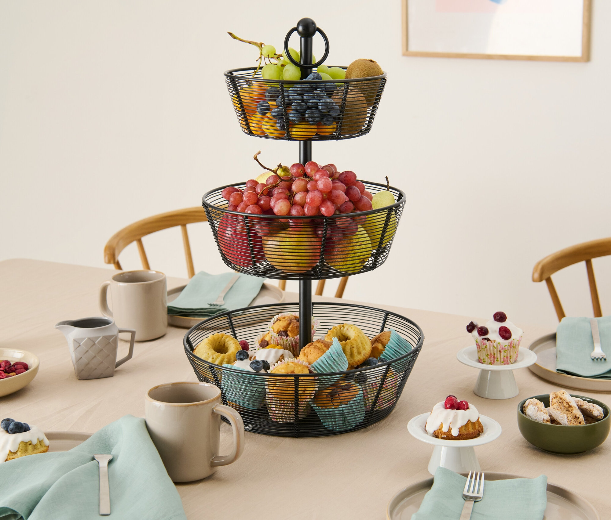 Na stole stojí třípatrový etažér s ovocem a muffiny.