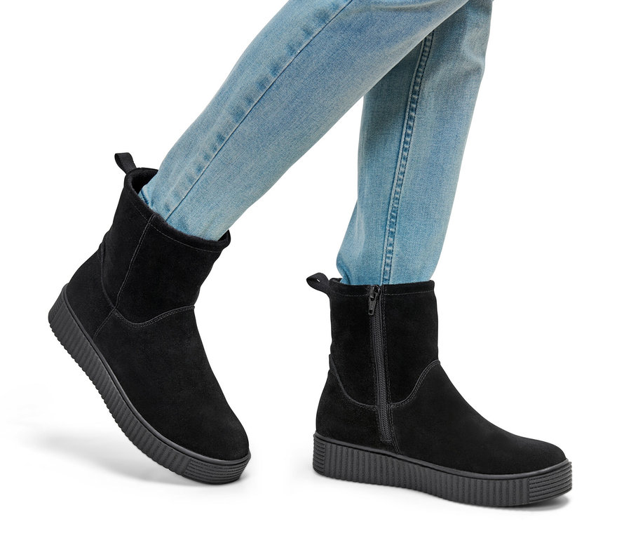 Nohy v džínových kalhotách a kotníkových botách ze semišové kůže.