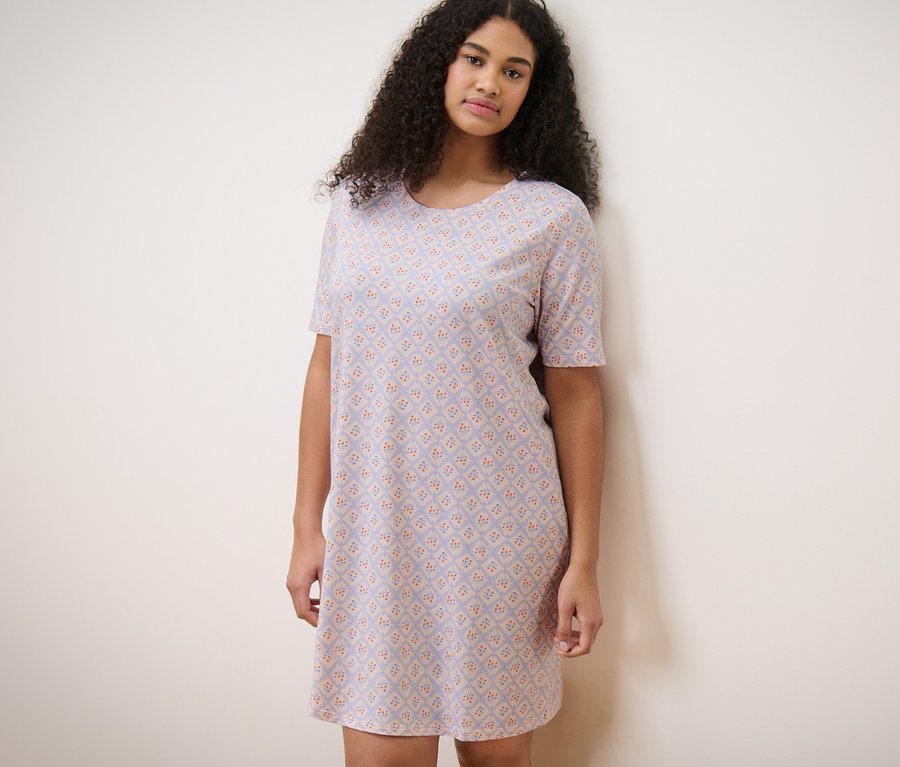 Žena v noční košili stojí u zdi.