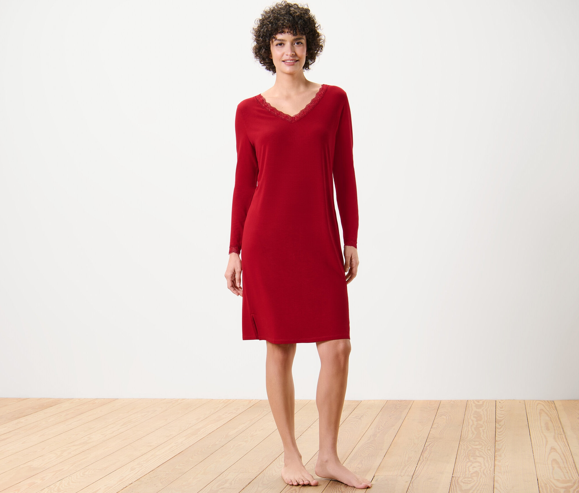 Žena stojí a má na sobě červenou noční košili s krajkovým lemováním.