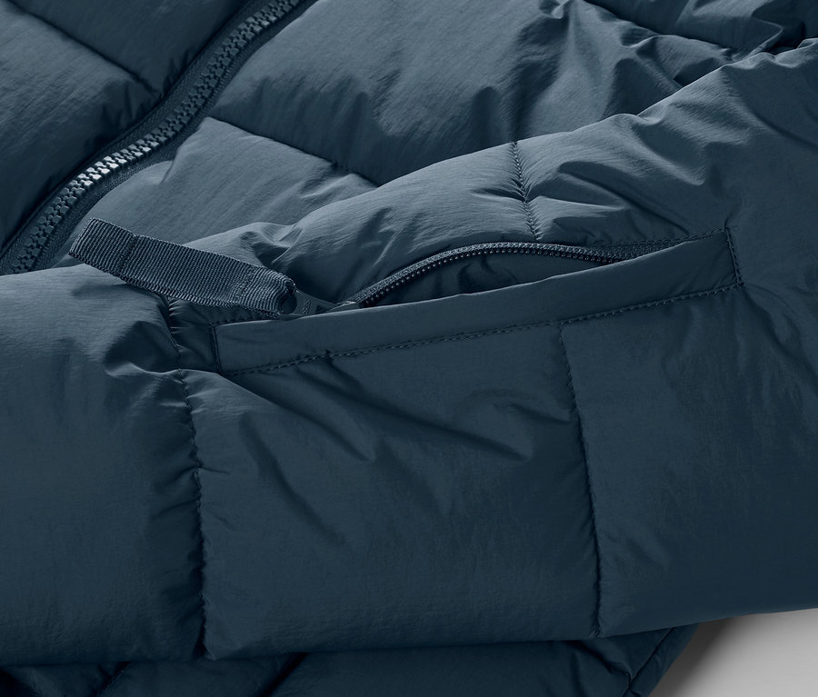 Detailní pohled na prošívanou lyžařskou bundu tmavě modré barvy, se zipem a kapsou.