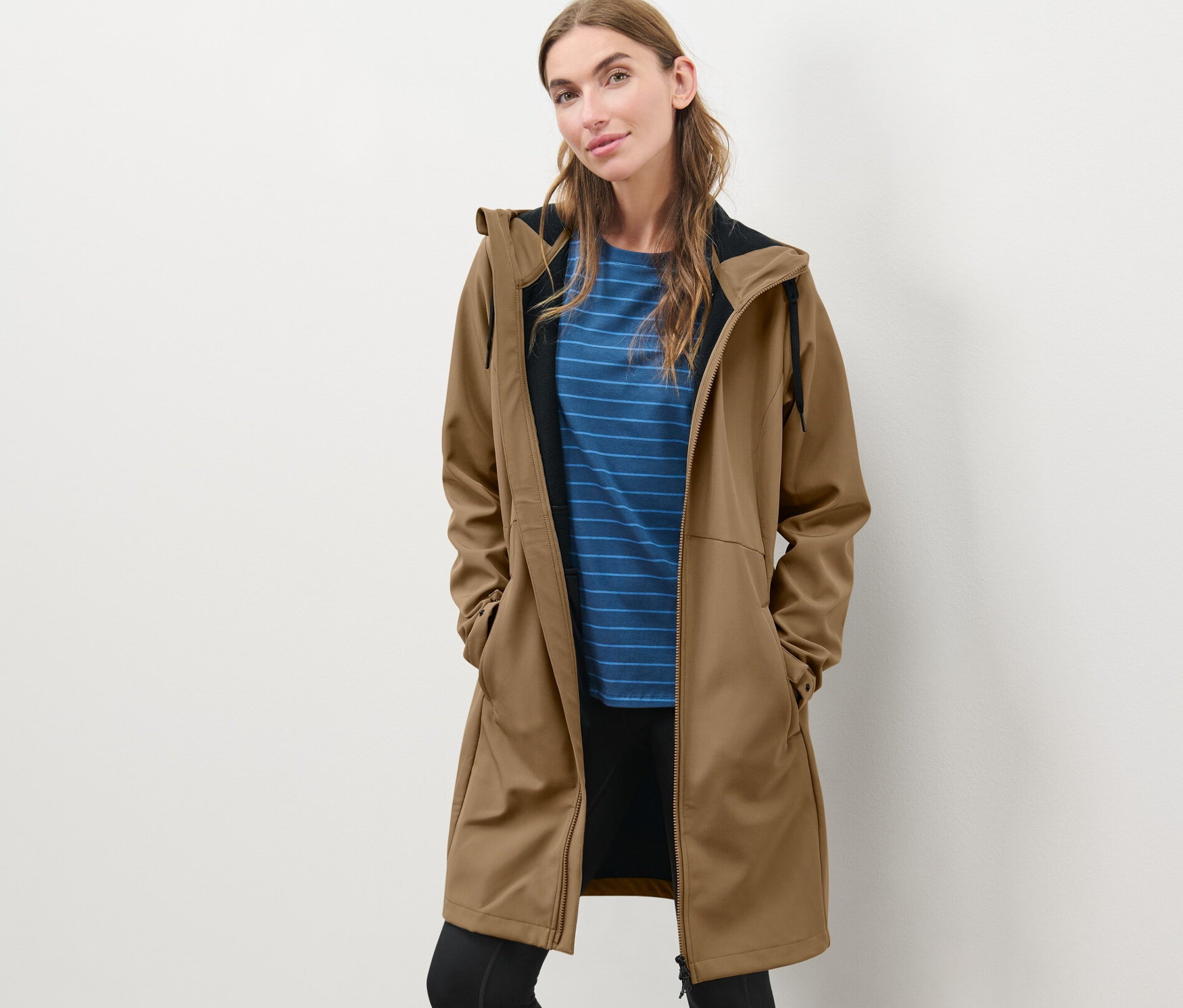 Žena pózuje v softshellovém kabátu nugátové barvy.
