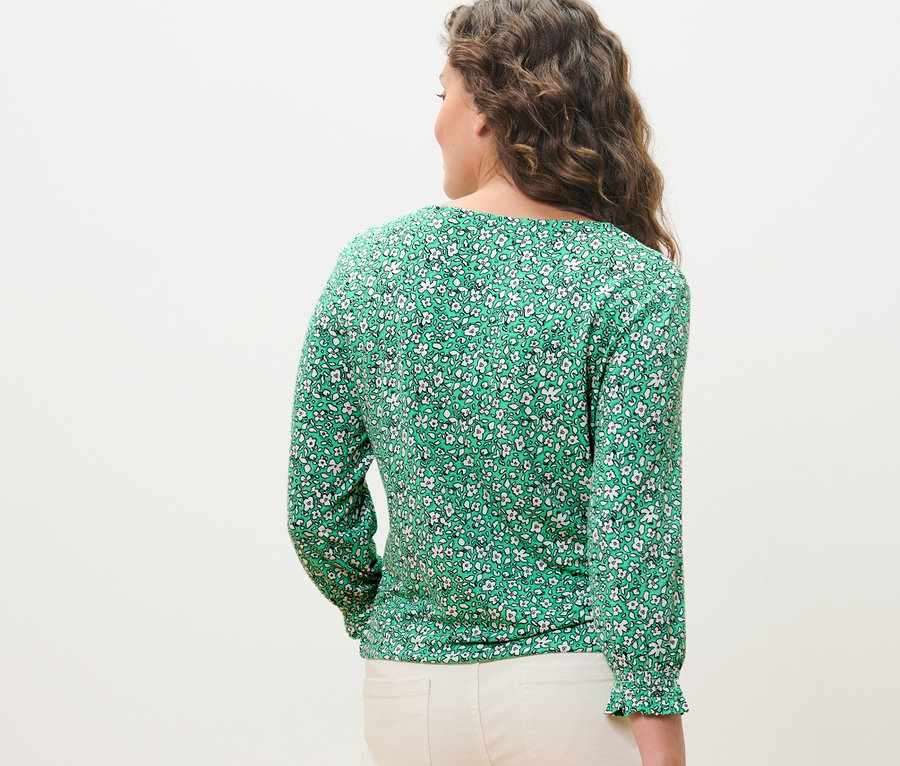 Žena, otočená zády, má na sobě zelené halenkové triko s potiskem.