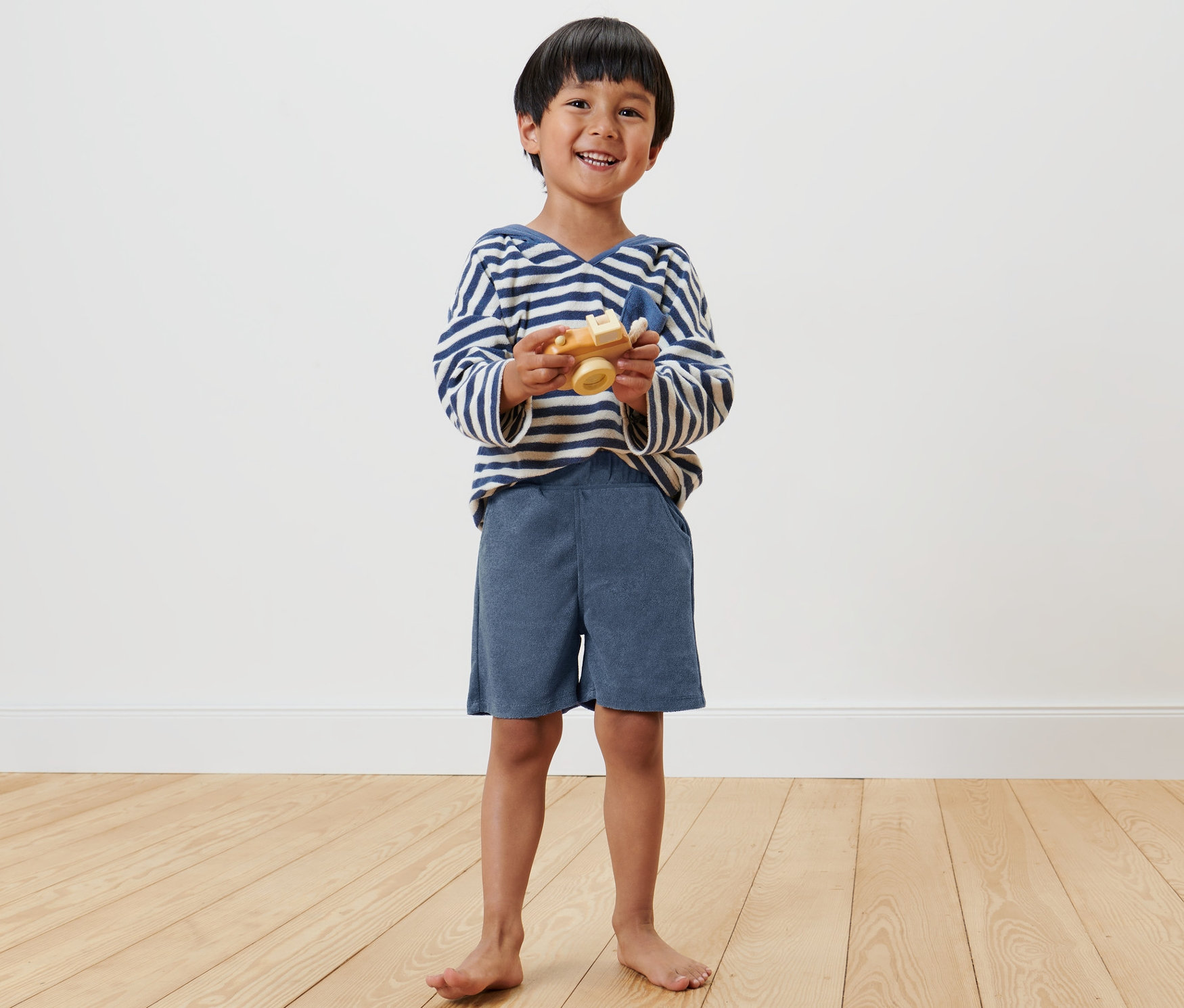 Usmívající se chlapec drží dřevěnou hračku letadlo a má na sobě dětské šortky, 2 ks.