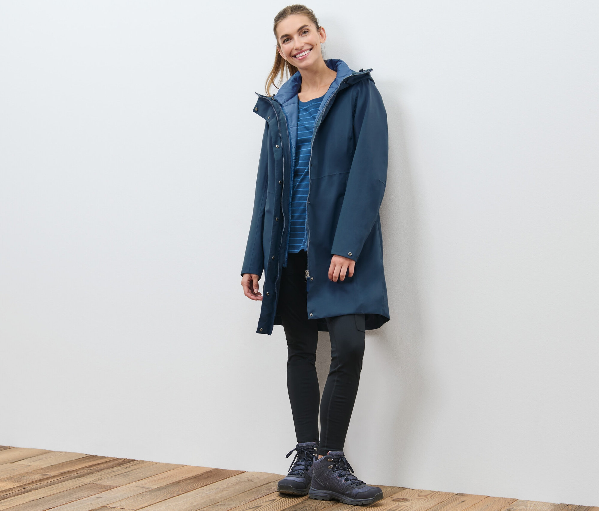 Žena stojí a pózuje v tmavě modrém funkčním kabátu 3 v 1 s vestou.